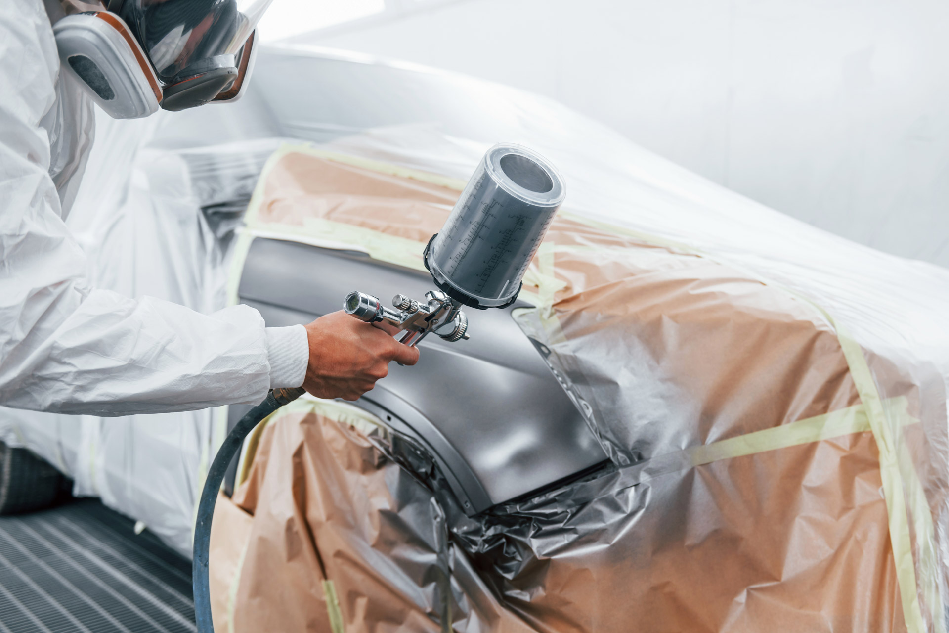 Painting job in progress. Caucasian automobile repairman in uniform works in garage